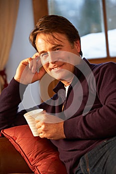 Middle Aged Man Relaxing With Hot Drink On Sofa