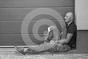 A middle-aged man is resting on the sidewalk. Portrait of caucasian bald man, outdoors. . Black and white