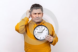 Middle aged man rubbing his head holding in hands big wallclock, has no time, worried about deadline photo
