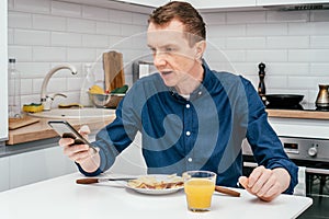 Middle-aged man with short ginger hair in blue shirt looking at mobile phone thunderstruck with news with arm raised.