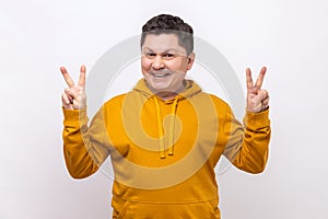 Middle aged man showing v sign to camera, winking and smiling, male wishing good luck, peace.