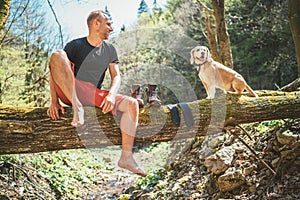 Middle-aged man sitting on the fallen tree log over the mountain forest stream and Smiling to beagle dog while he waiting for