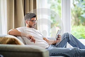 Middle-aged man sitting at home on the sofa and holding digital tablet in his hand