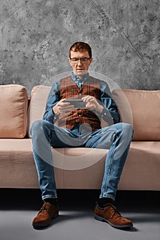 Middle aged man sitting on sofa and watching video on smartphone