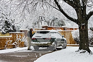 Middle aged man with snow covered car in driveway on extremely snowy day with snow falling