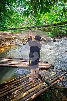 A middle aged man standing on bamboo raft at the river stream in Malaysia