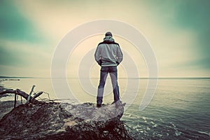 Middle-aged man standing on broken tree on wild beach looking at sea horizon