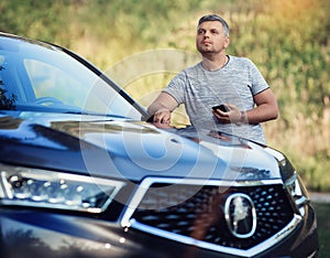 A middle-aged man is standing near the car. Muccina speaks on the phone. Dear beautiful car. The man is calm and confident.