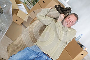 Middle-aged man struggling to carry woven rug