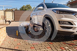 A middle-aged man teaches children of boys 4 and 10 years old to wash a car in the yard of his house on a summer sunny day. 2019.