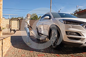 A middle-aged man teaches children of boys 4 and 10 years old to wash a car in the yard of his house on a summer sunny day. 2019.