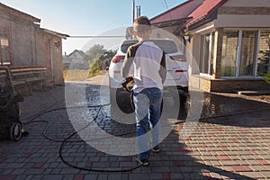 A middle-aged man teaches children of boys 4 and 10 years old to wash a car in the yard of his house on a summer sunny day. 2019.