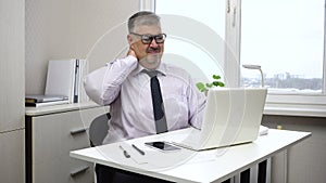 A middle-aged man is tired from working at the computer and rubs his stiff neck