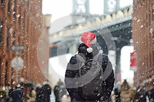 Middle aged man tourist in a Santa Claus hat is walking during a snowfall near Manhattan Bridge in New York on a snowy Christmas