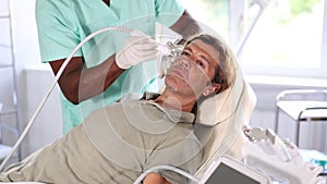 Middle-aged man undergoing skin therapy session in modern cosmetology clinic. Aesthetician applying atomized nutrients