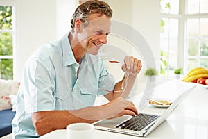 Middle Aged Man Using Laptop Over Breakfast