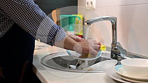 A middle-aged man washes dirty dishes in his home kitchen. A man is doing household chores