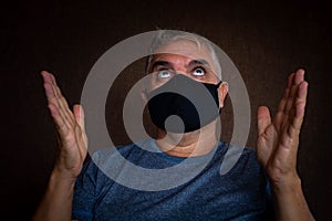 Middle-aged man with white hair and face mask in times of pandemic. With the hands towards the sky imploring