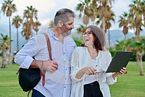 Middle-aged man and woman looking into the laptop screen outdoors