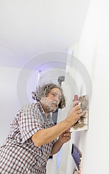 Middle-aged man worker, builder or homeowner plastering a white
