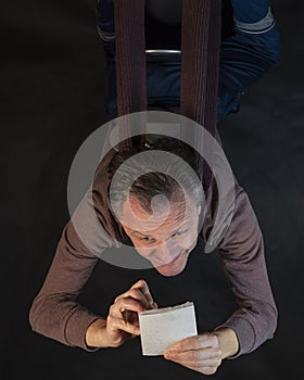 Middle-aged man writes notes on a small notepad sitting upside down with funny expression