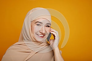 Middle aged mature Muslim Woman Using Mobile Phone standing over yellow background. Free technology lifestyle muslim concept
