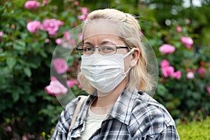 Middle aged mixed race blonde woman with eyeglasses wearing white surgical mask.
