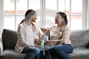 Middle-aged mom and adult daughter relax talk at home