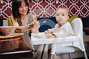 Middle aged mother feeding her infant baby with the spoon in a cafe