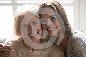 Middle aged mother grown up daughter embracing looking at camera