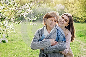 Middle-aged mother and her daughter hugging in blooming garden