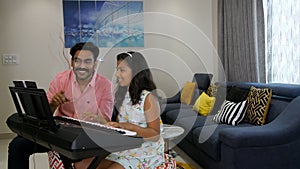 A middle-aged music teacher training an Indian girl on keyboard / piano - musical instrument, father-daughter bonding