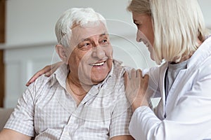 Middle-aged nurse hug elderly man patient sitting on couch