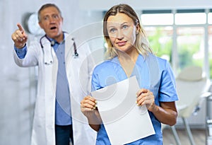 Upset middle-aged nurse standing with her back to angry doctor