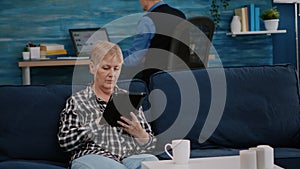 Middle aged old woman relaxing holding tablet reading e book