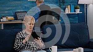 Middle aged old woman relaxing holding tablet reading e book