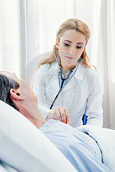 Middle aged patient lying on bed and doctor examining him with stethoscope