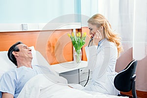 Middle aged patient lying on bed and doctor examining him with stethoscope