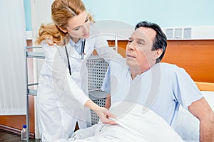 Middle aged patient with pain sitting on bed, doctor helping him