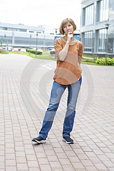 A middle-aged redhead woman in casual clothes stands in the street, lost in thought