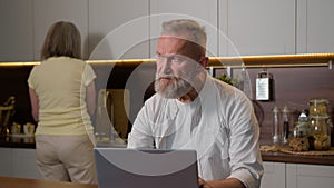 Middle aged retired 50s man husband gray-haired businessman thinking working distant with computer notebook thoughtful