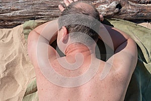 Middle aged male lying on sandy beach outdoors. The sun shines on his body