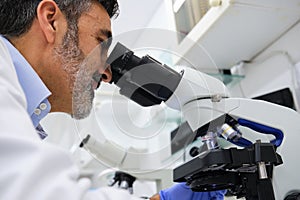 Middle aged scientist looking through microscope in a laboratory.