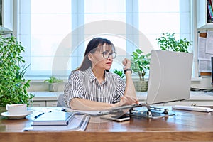 Middle-aged serious woman working at computer laptop in home office