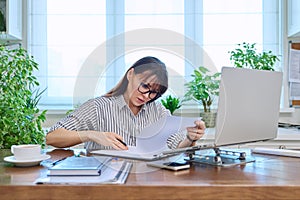 Middle-aged serious woman working at computer laptop in home office