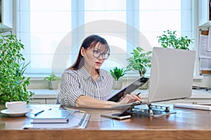 Middle-aged serious woman working at computer laptop in home office