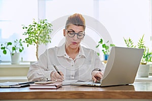 Middle-aged serious woman working at computer laptop in home office