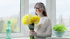 Middle aged smiling woman with bouquet of flowers, near window