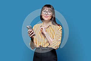 Middle aged smiling woman with smartphone on blue studio background