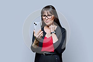 Middle aged smiling woman using smartphone on grey studio background